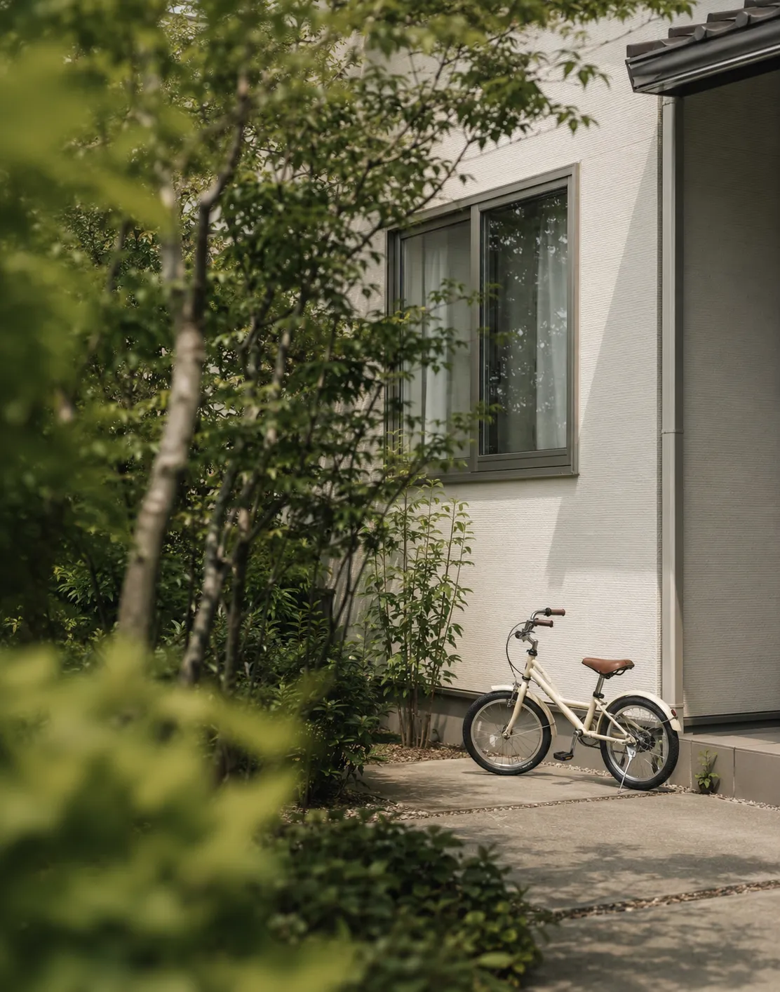 緑越しに見える住宅の側面。土間の通路に子ども用の自転車が置かれている
